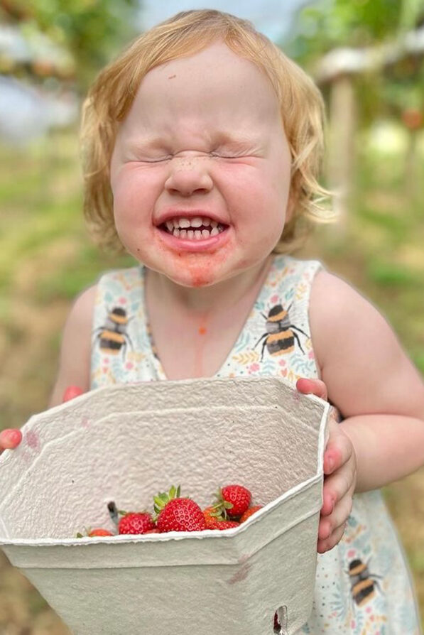 A child looking overwhelmingly happy with her punnet of strawberries